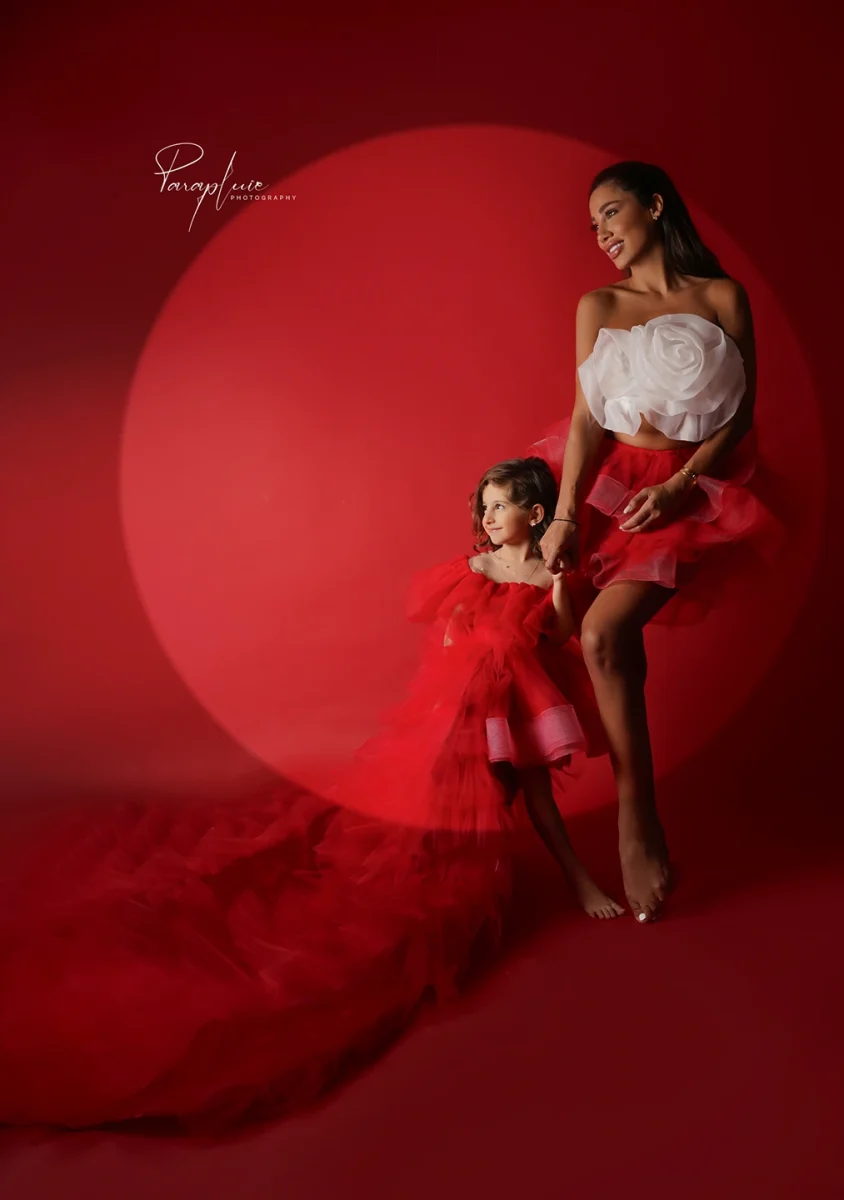 Mother and daughter in matching red and white couture dresses posing on a red backdrop, fine art family photoshoot at Parapluie Studio Lebanon.