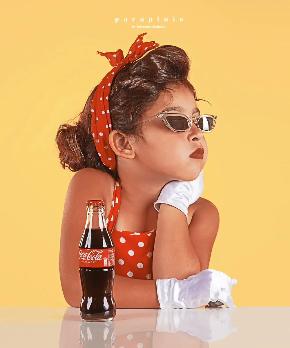 Young girl in retro polka dot outfit with sunglasses and gloves posing beside a Coca-Cola bottle, vintage-inspired children’s photoshoot at Parapluie Studio Lebanon.