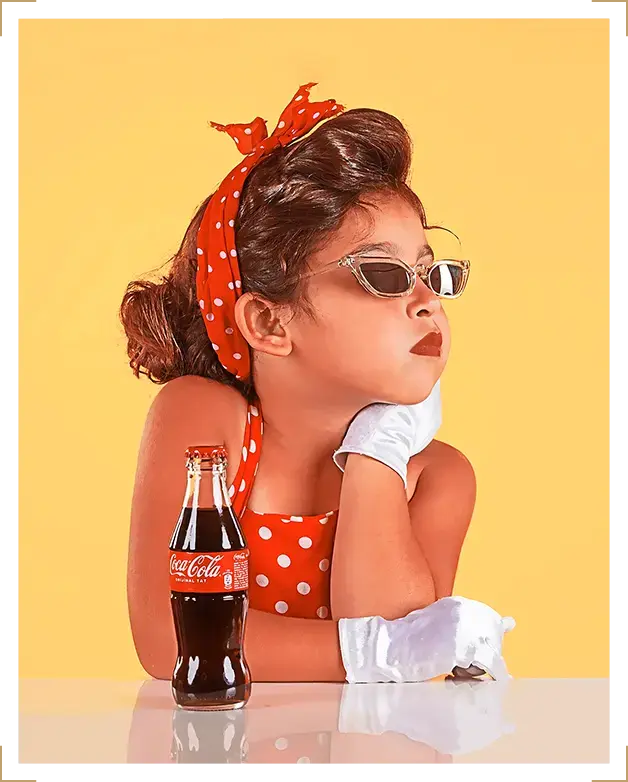 Young girl in retro polka dot outfit with sunglasses and gloves posing beside a Coca-Cola bottle, vintage children’s photoshoot at Parapluie Studio Lebanon.